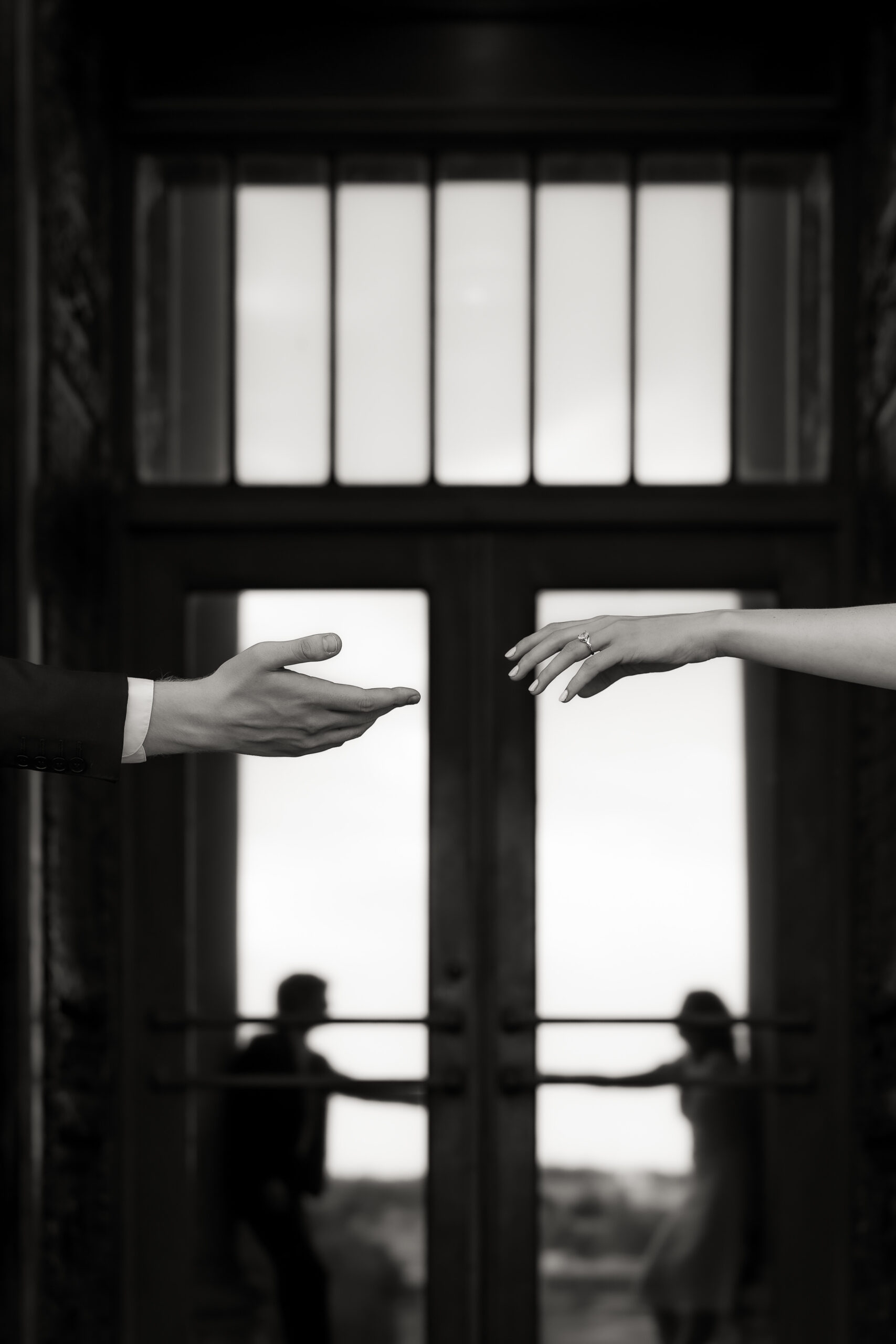 Black and white photograph of hands reaching for one another in front of the Nelson Atkins in Kansas City, Missouri. Photographed by destination wedding photographer, Samantha Mudd Photo.